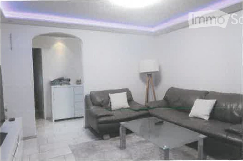 Modern living room with a grey sectional sofa, white throw pillows, a glass coffee table, a floor lamp, and a small white cabinet in the background.