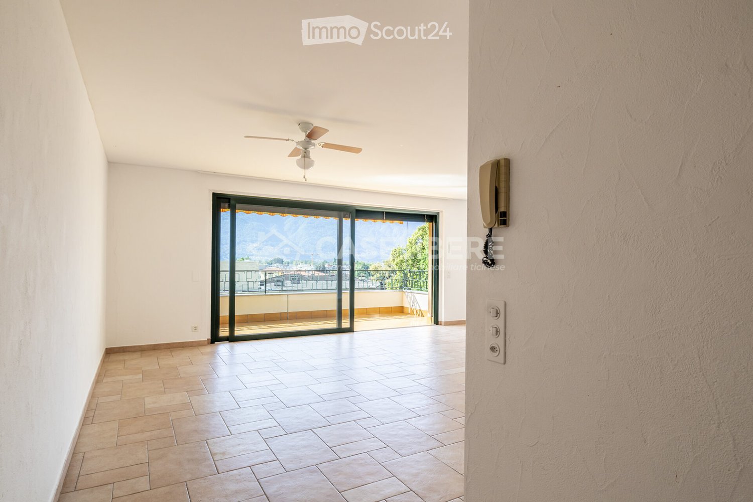 Empty hallway with tiled floor, white walls, ceiling fan, and large sliding glass door leading to a balcony with a scenic view.