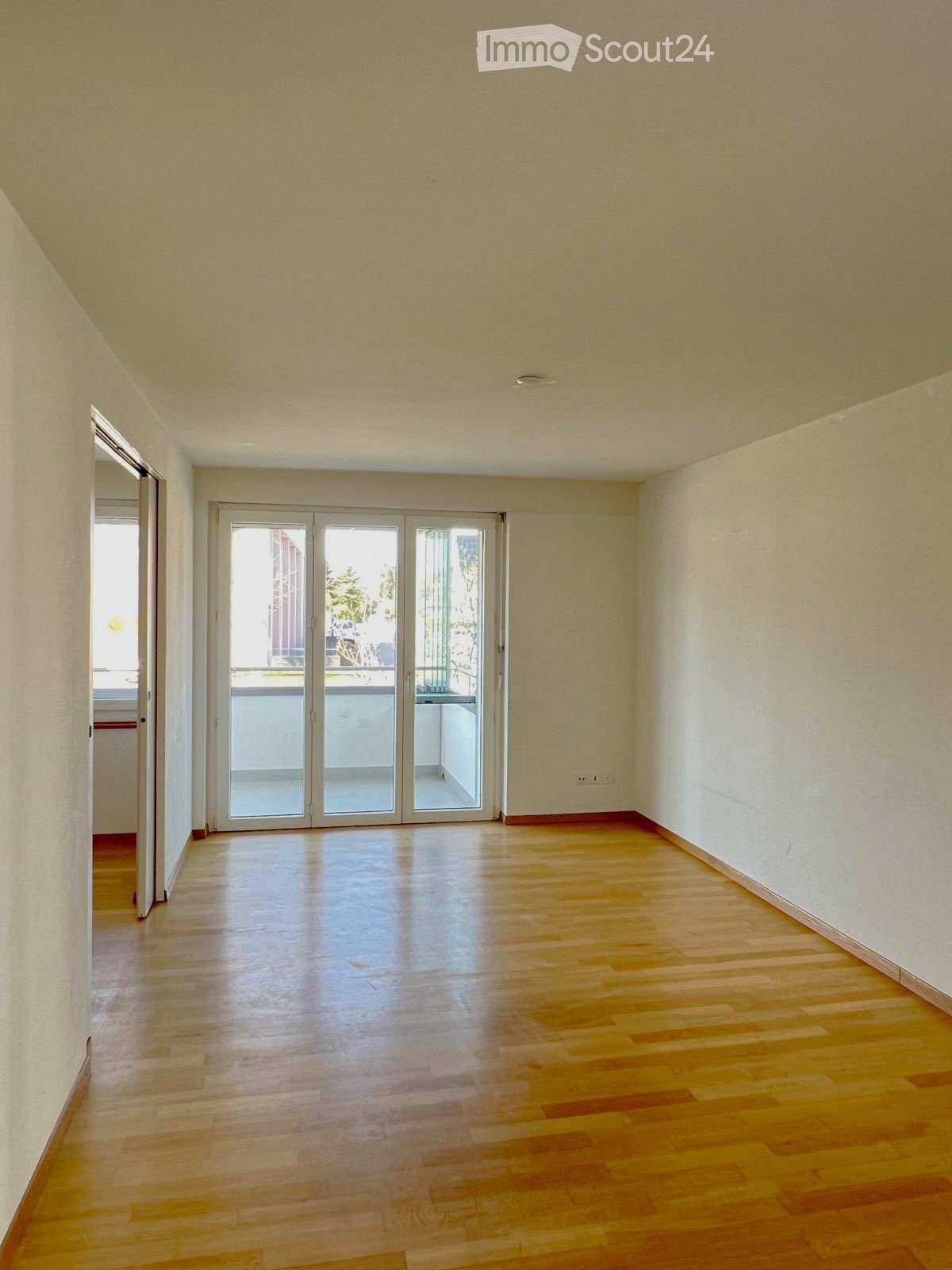 Empty room with wooden flooring, white walls, and large sliding glass doors leading to a balcony.