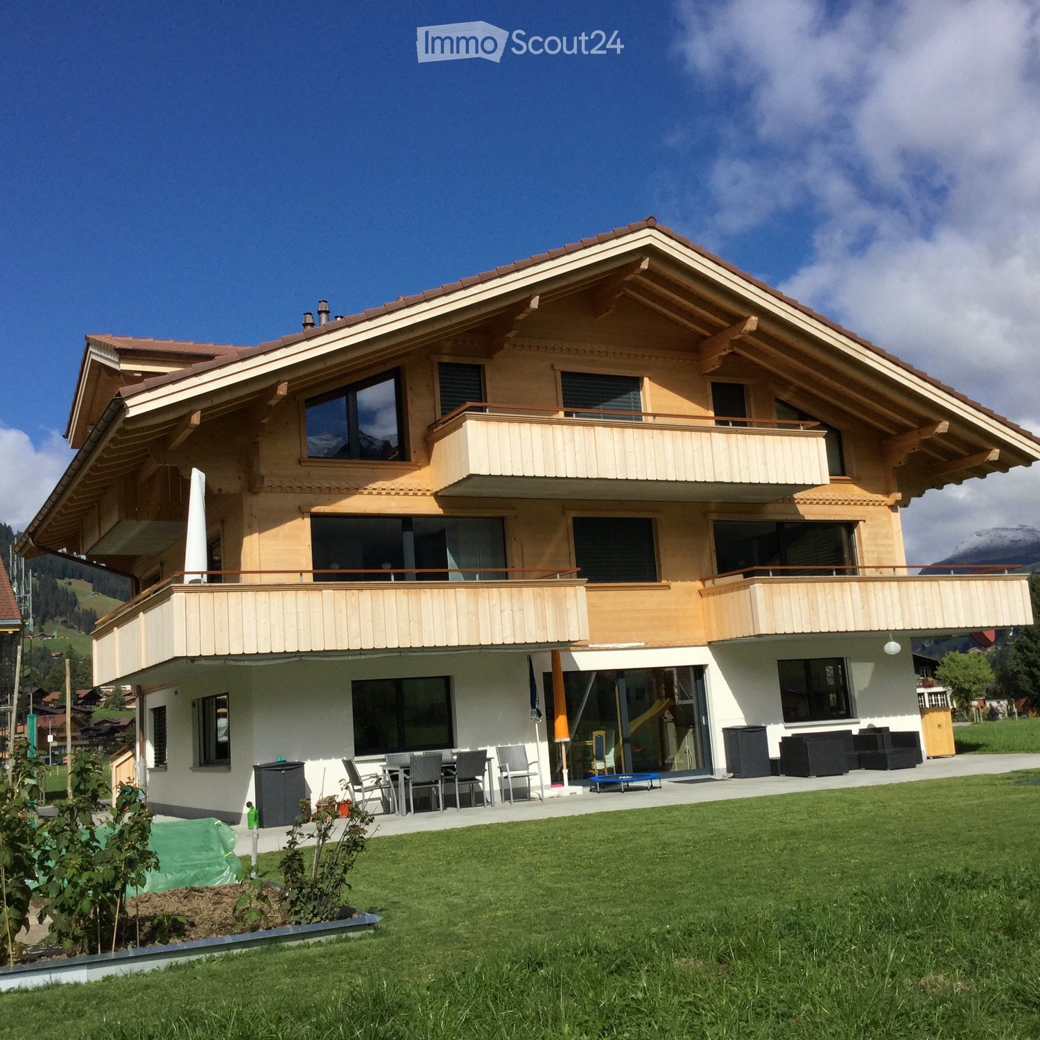Two-story house with wooden balconies, large windows, and a well-maintained lawn.