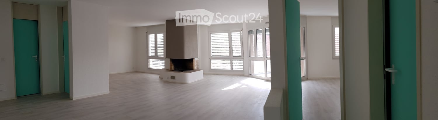 Empty room with wooden flooring, white walls, large windows with blinds, and a fireplace in the center.