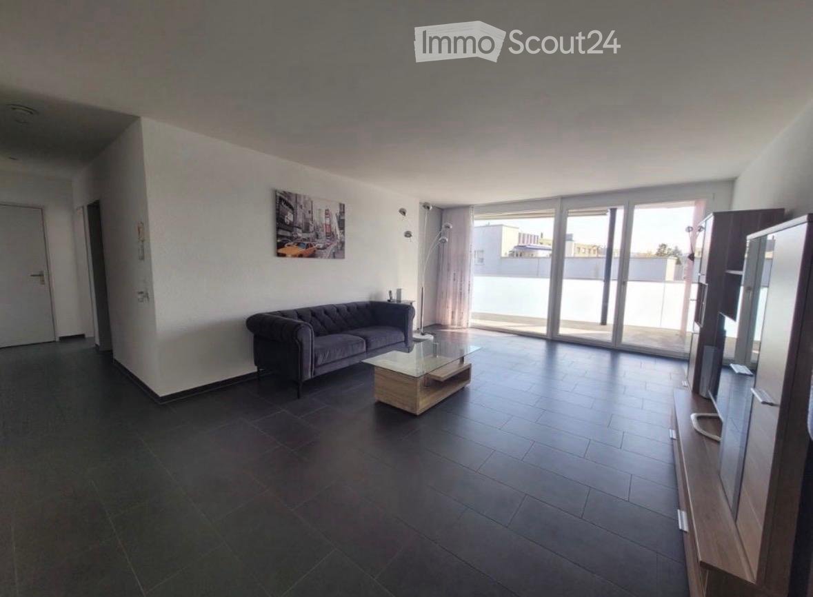 Modern living room with dark tiled flooring, grey sofa, glass coffee table, TV stand, and large sliding glass doors leading to a balcony.