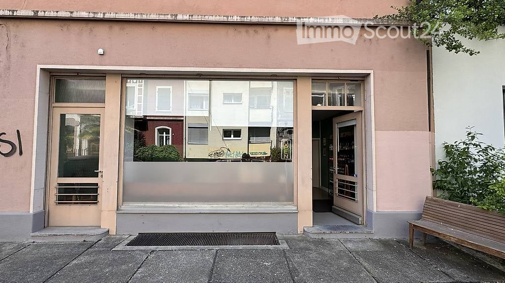 Facade of a commercial building with glass storefront and entrance, adjacent to a wooden bench.