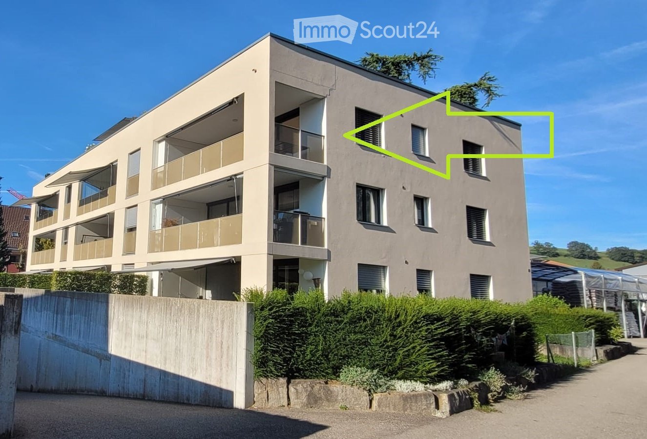 Modern multi-story residential building with balconies, large windows, and a landscaped front yard.