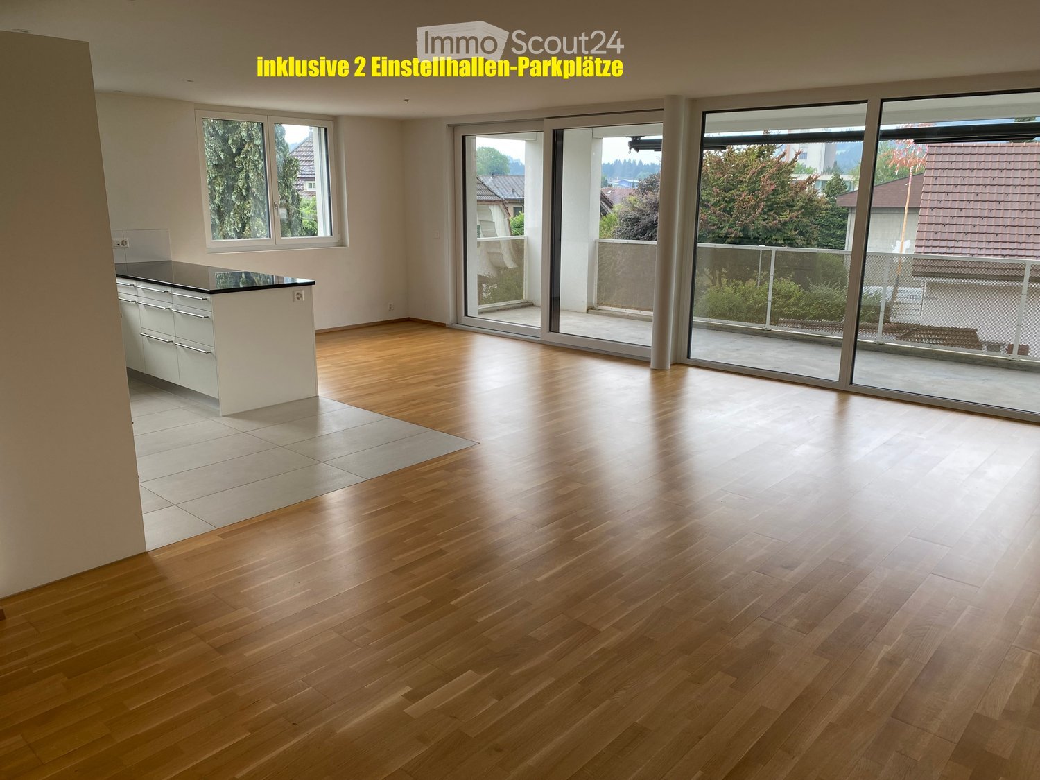 Empty room with wooden flooring, white walls, large windows, and sliding glass doors leading to a balcony.