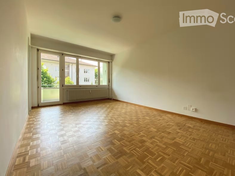 Empty room with wooden parquet flooring, large windows, and white walls. No furniture or equipment present.