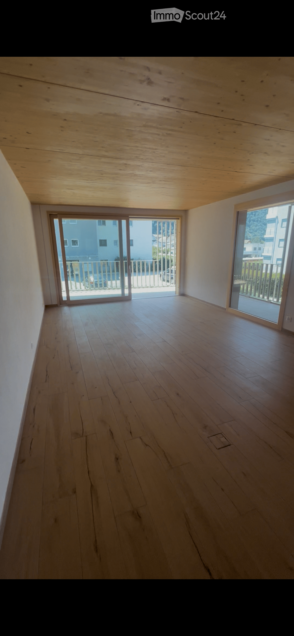 Empty room with wooden flooring and white walls, featuring large sliding glass doors leading to a balcony area.