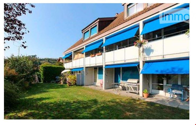 A multi-story residential building with blue awnings, balconies, and a well-maintained lawn in front.