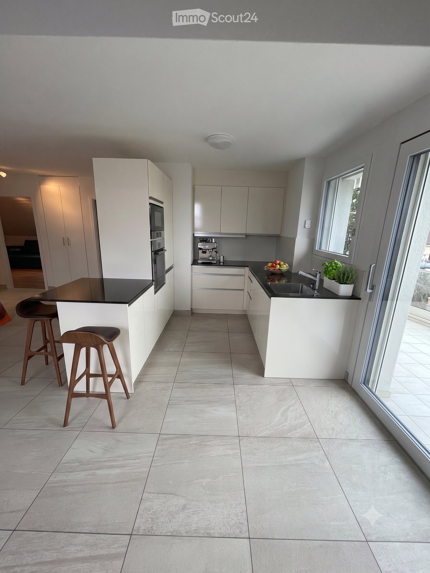 Modern kitchen with white cabinets, black countertops, a central island with two stools, a sink with a faucet, and a coffee machine on the counter.
