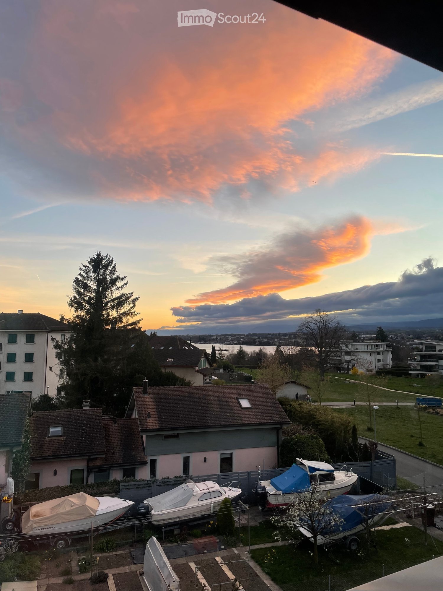 Balcony view overlooking a residential area with boats on trailers, houses, and a sunset sky.