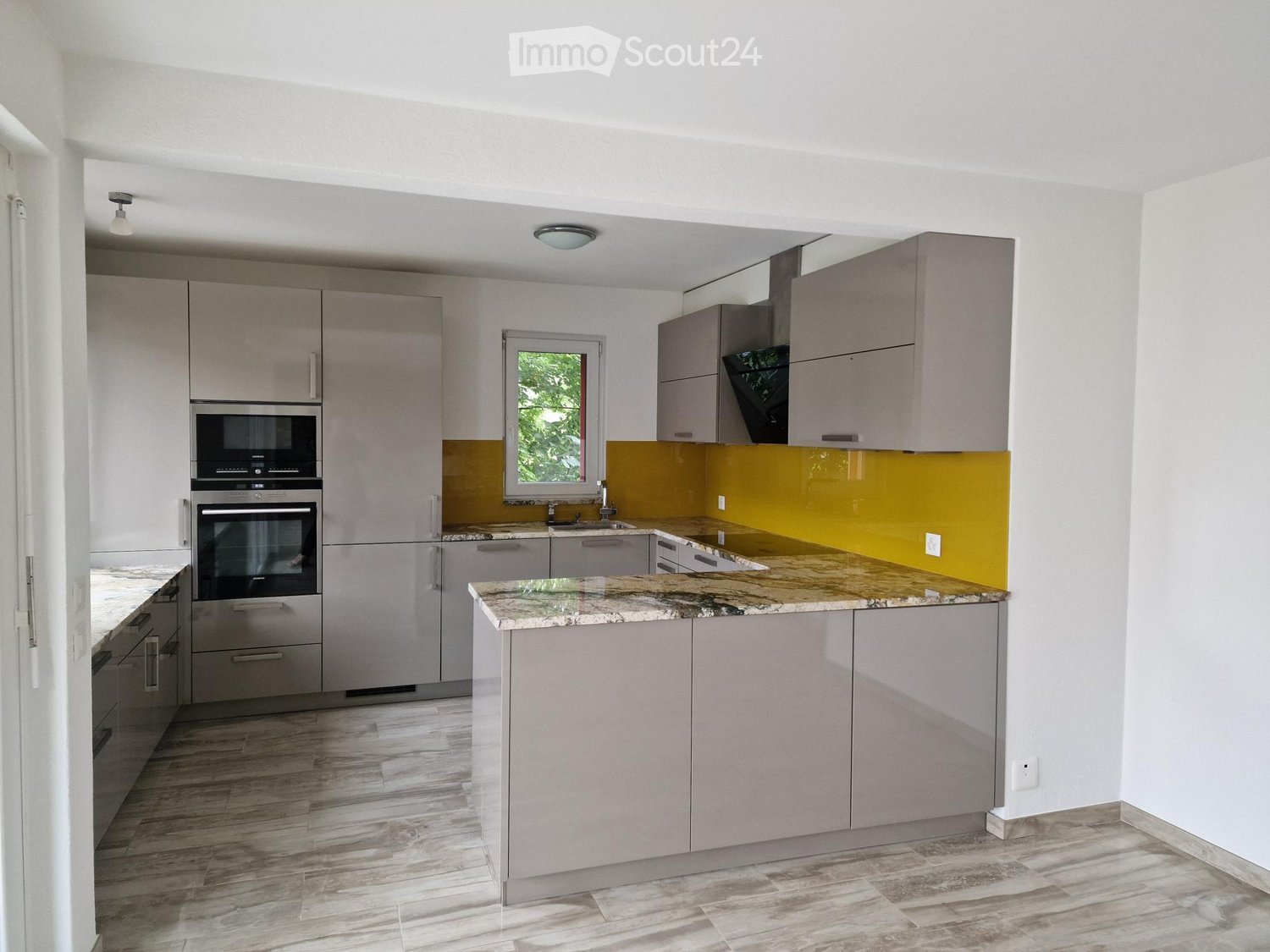 Modern kitchen with grey cabinets, marble countertops, stainless steel appliances, and a yellow backsplash.