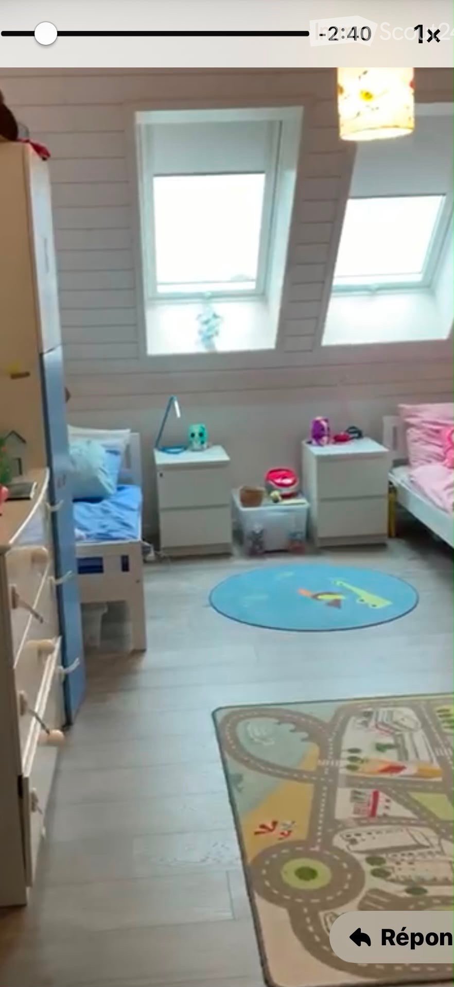 Cozy children's bedroom with two single beds, nightstands, a colorful play rug, and a toy train track mat on the floor.
