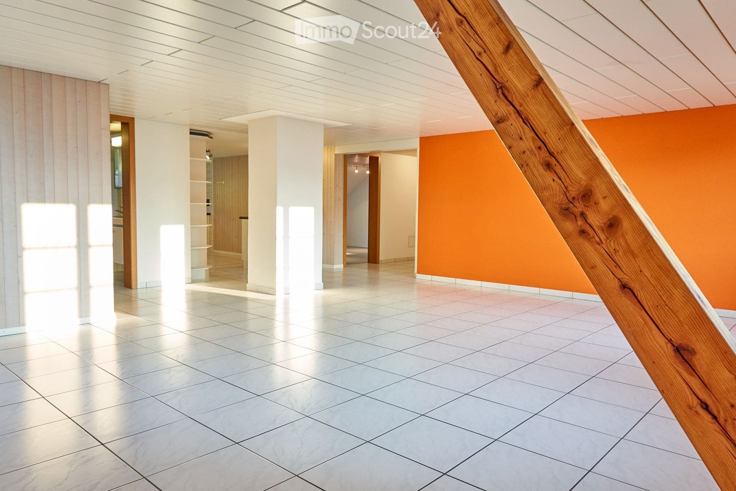 Bright, modern hallway with white tiled flooring, white walls, and a wooden staircase leading upwards. Features include recessed lighting, white columns, and an orange accent wall on one side.