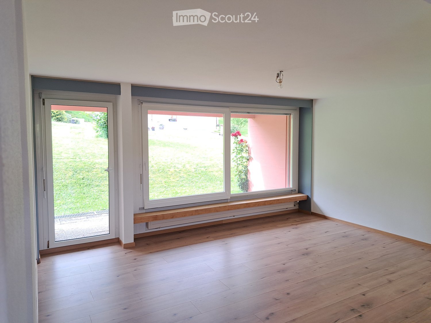 Empty room with wooden flooring, large windows, and a bench beneath the windows.