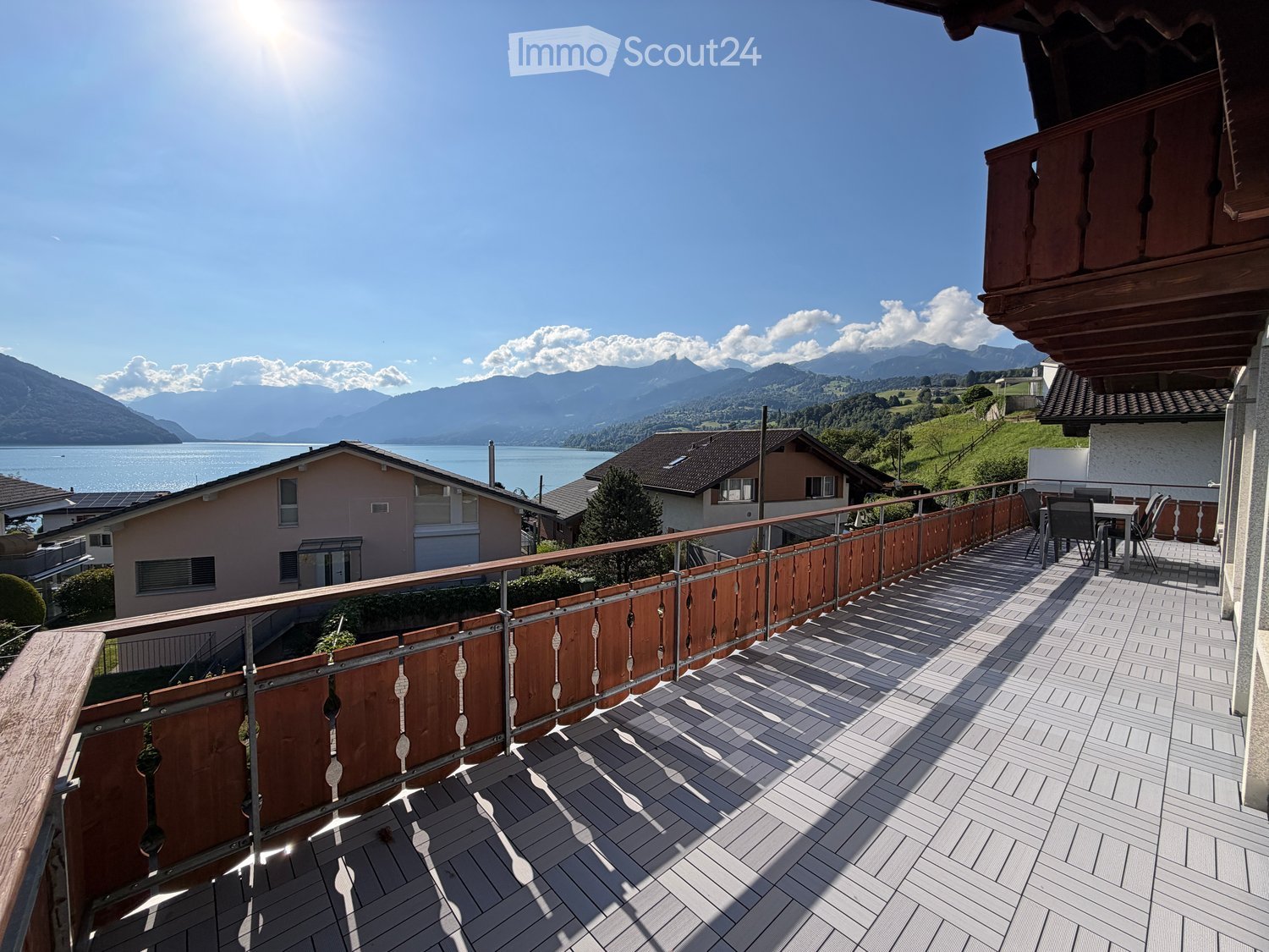 Balcony with wooden decking, metal railing, and outdoor furniture overlooking a scenic lake and mountain view.