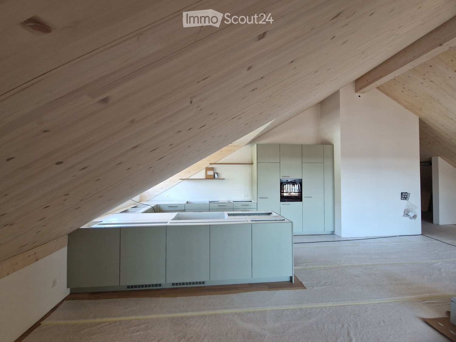 Modern kitchen with light grey cabinets, a central island, and a built-in oven, featuring exposed wooden beams and a skylight.