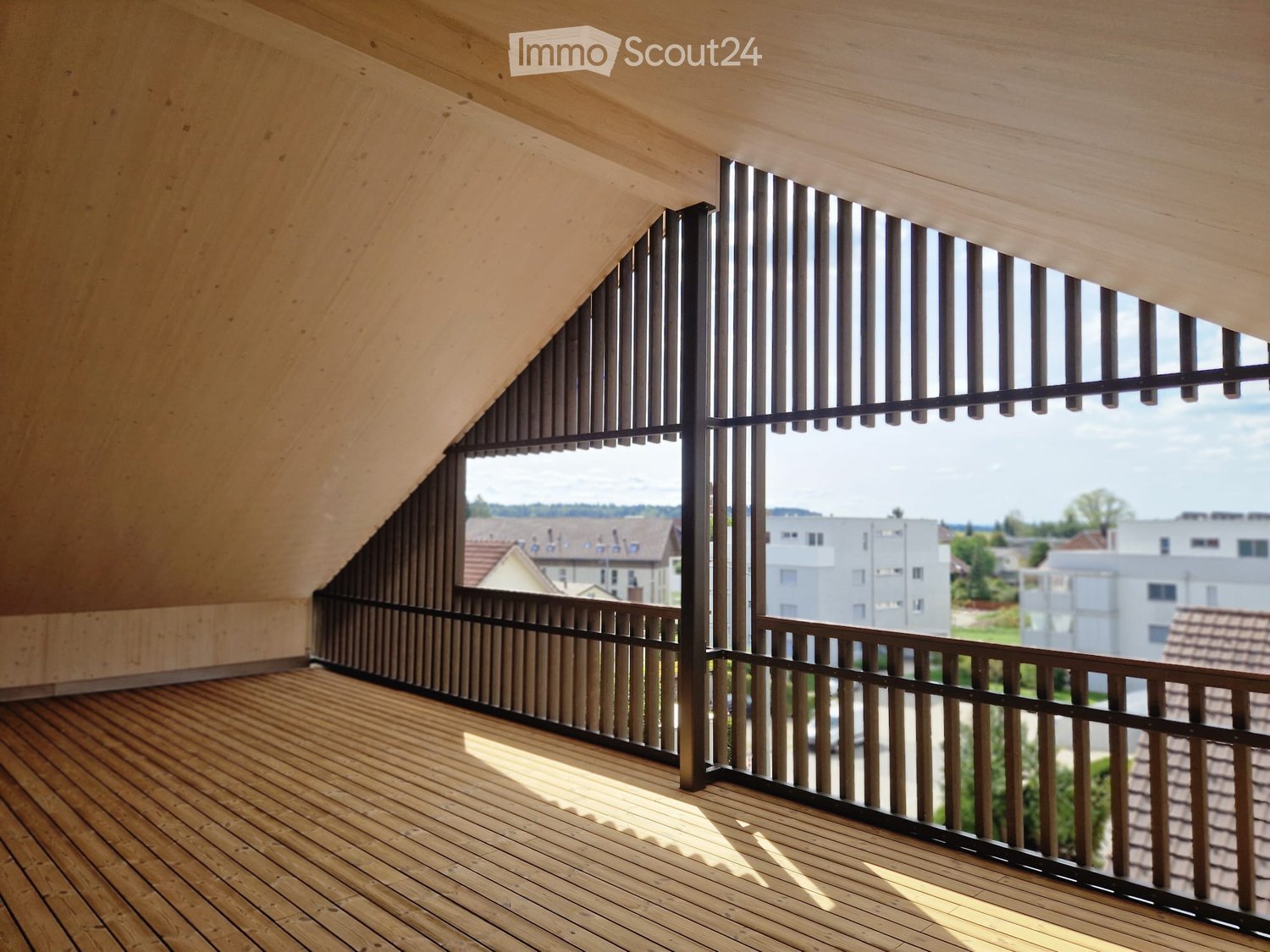 Wooden balcony with slatted railing and large windows overlooking a residential area.