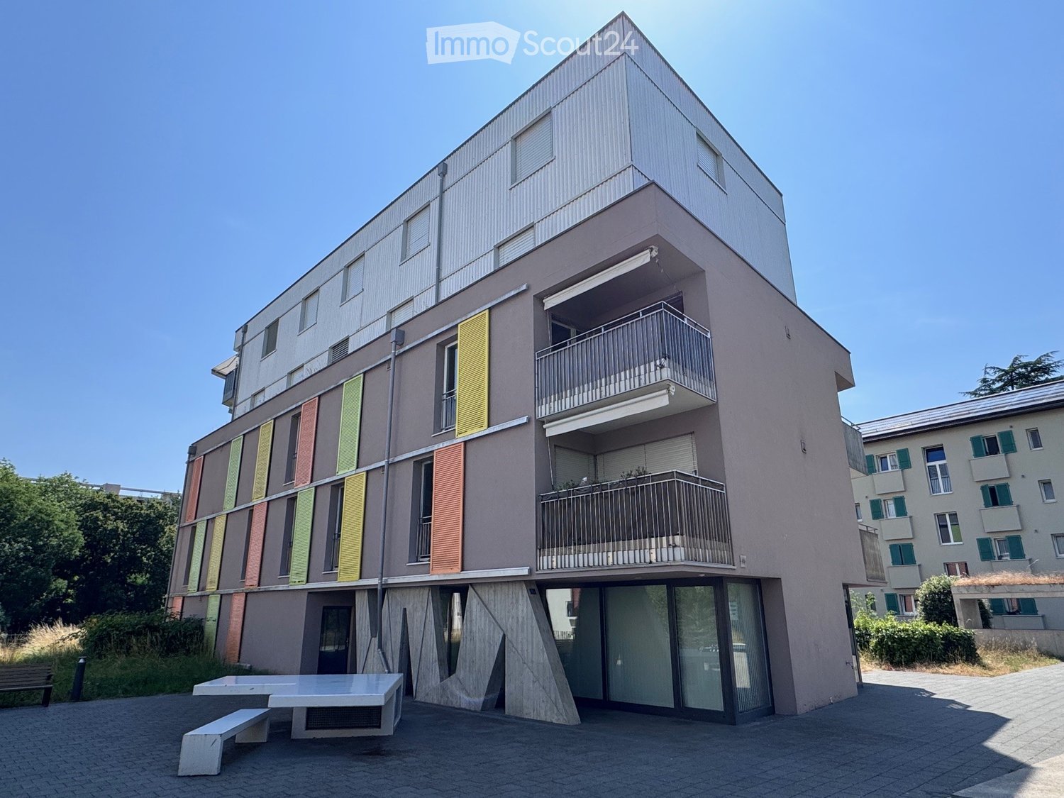 Modern multi-story building with colorful shutters, balconies, and a raised ground floor entrance.