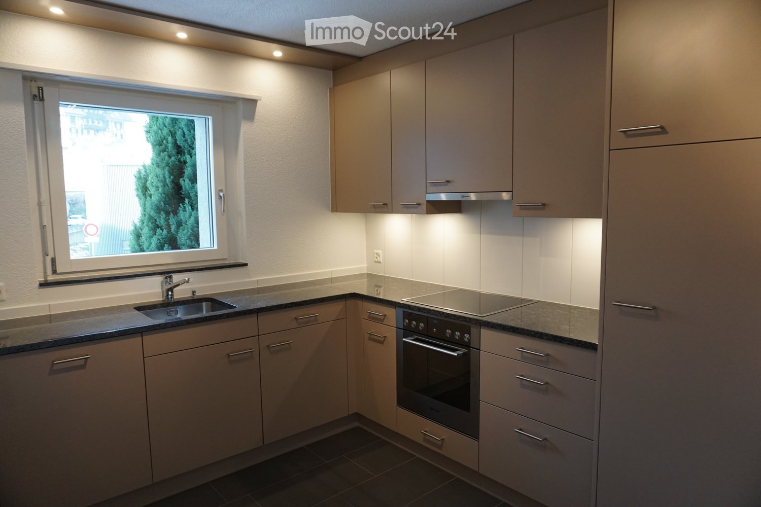 Modern kitchen with light-colored cabinets, stainless steel appliances, and a window overlooking greenery.