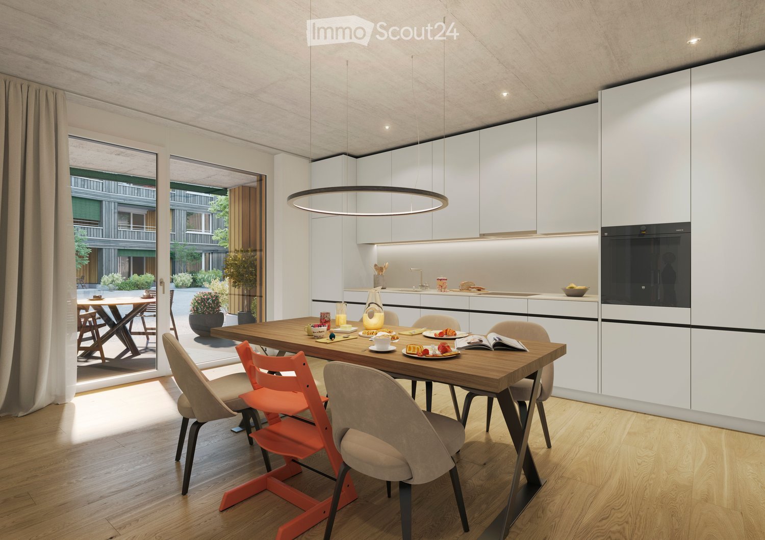 Modern kitchen with white cabinets, a wooden dining table, and a pendant light. The table is set with plates, cups, and a book, and there are chairs around it. An oven is visible in the background, and the space has large windows with a view of the outdoo