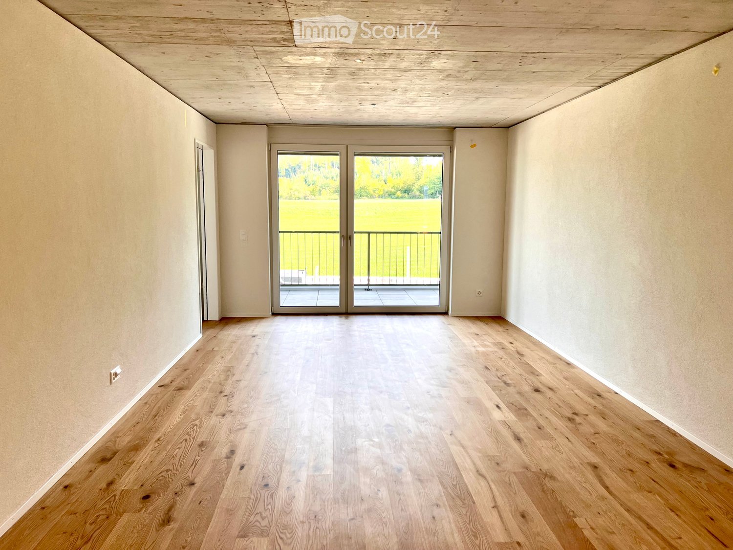 Empty room with light wooden flooring, white walls, and a large sliding glass door leading to a balcony.