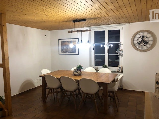 Dining room with wooden table, white chairs, pendant light fixture, picture frame on wall, and decorative clock.