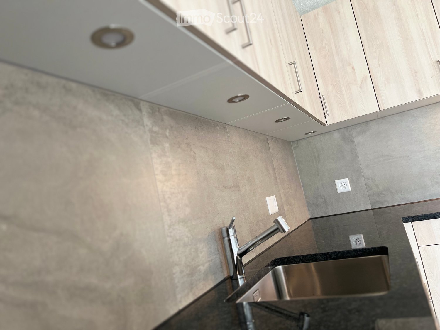 Modern kitchen with light wood cabinets, stainless steel sink, and sleek faucet.