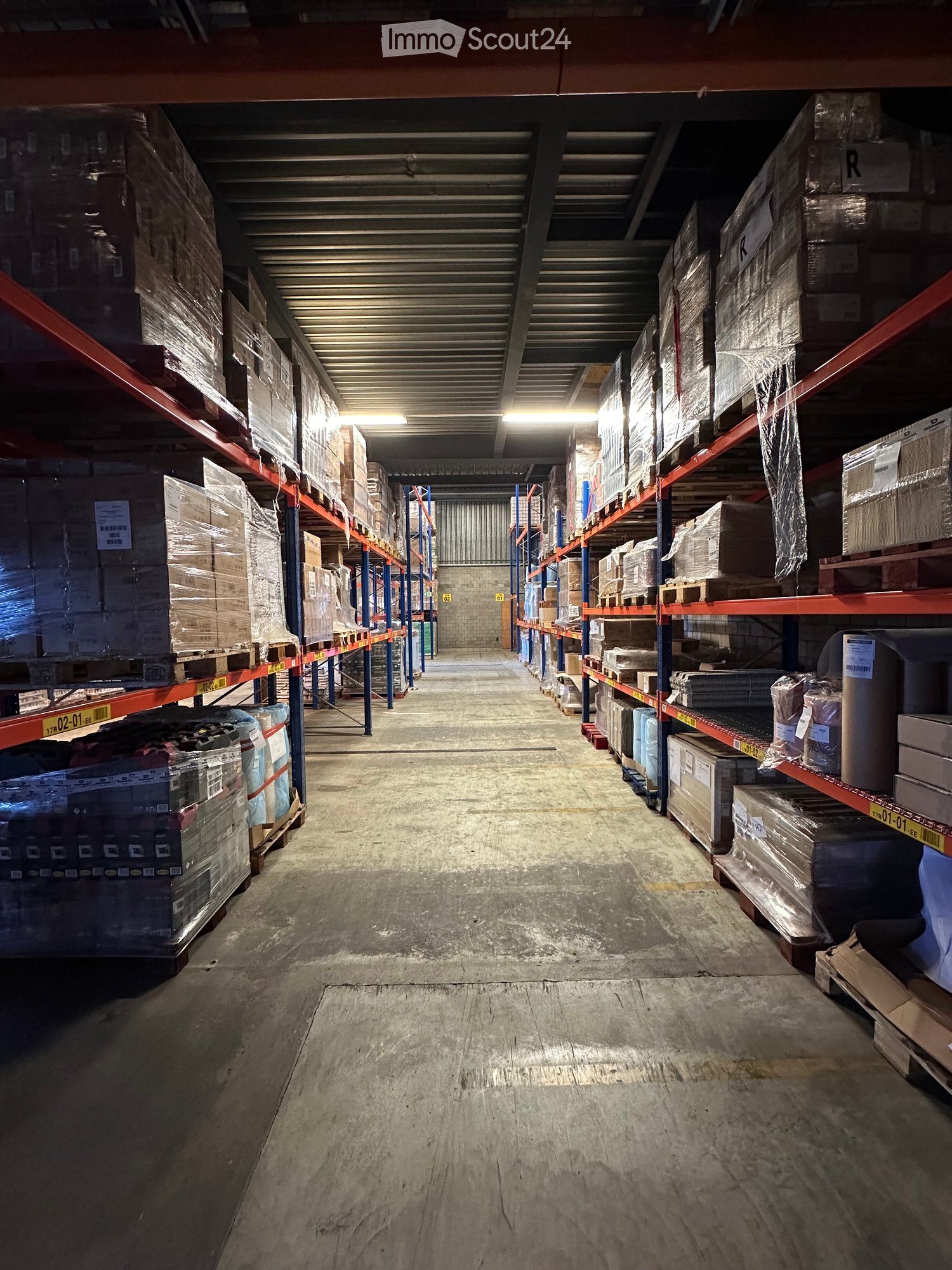 Warehouse interior with metal shelving units filled with various boxes and packages, concrete floor, and industrial lighting.
