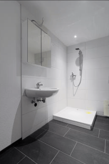 Modern bathroom with white tiles, black floor tiles, a white sink, a mirror, and a shower area.