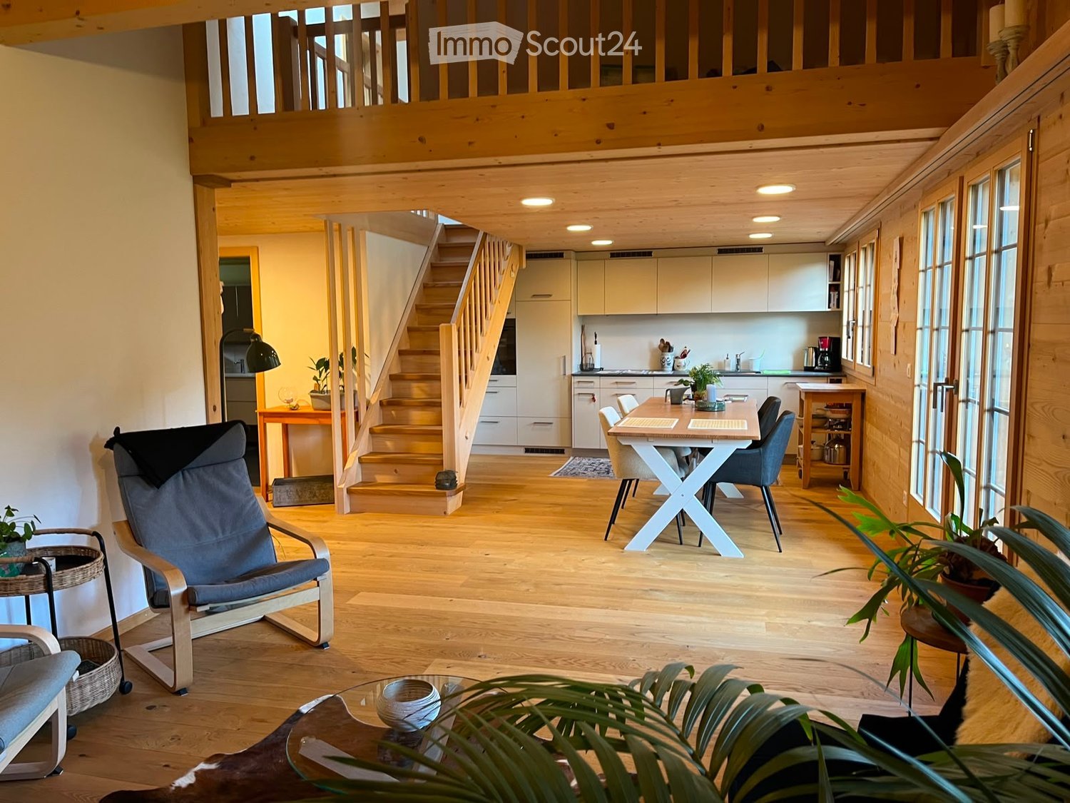 Open-plan living and dining area with wooden flooring, a staircase leading to an upper level, a modern kitchen, and comfortable seating.
