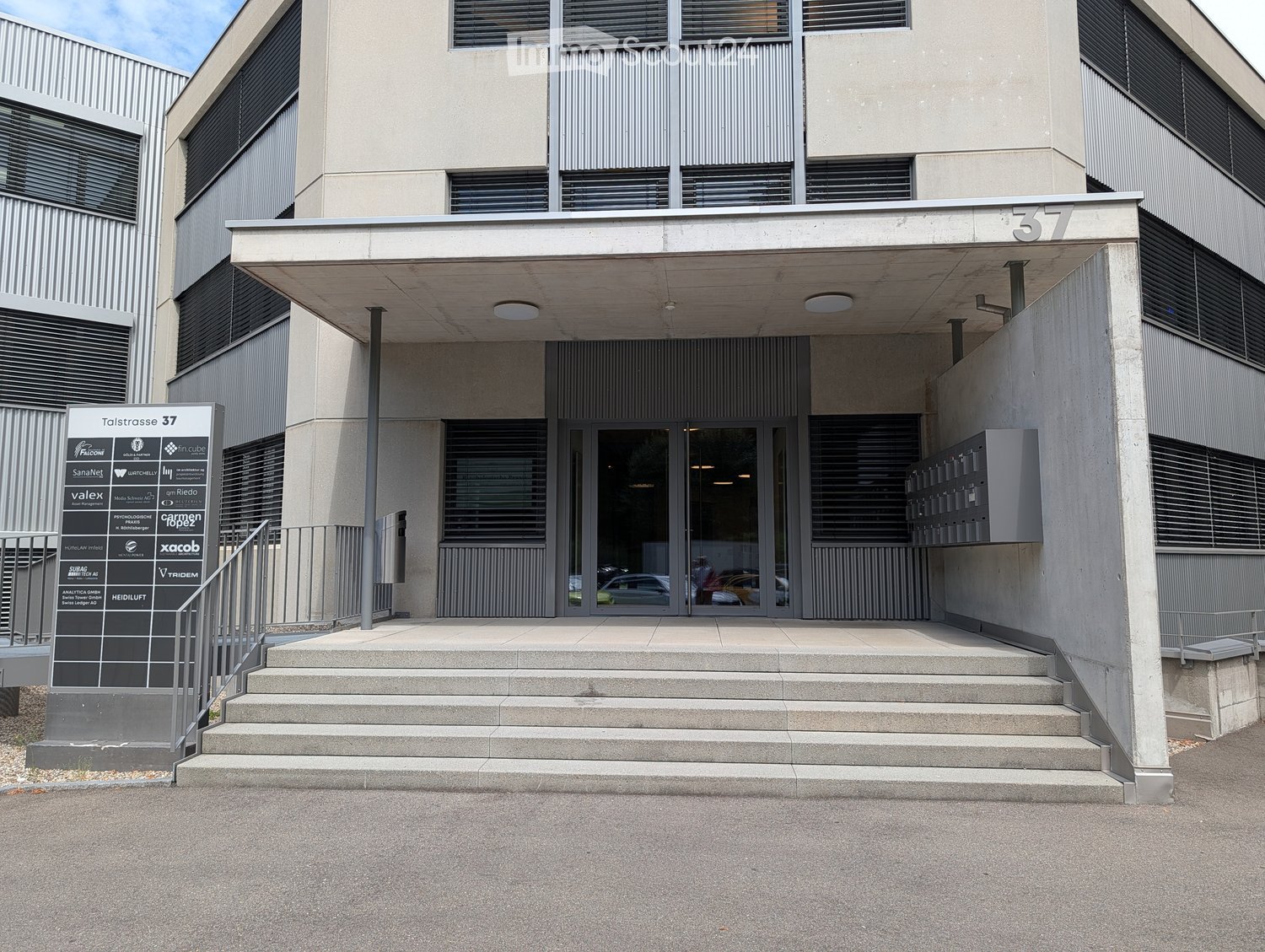 Modern building entrance with concrete steps, glass doors, and a sign displaying "Talstrasse 37".