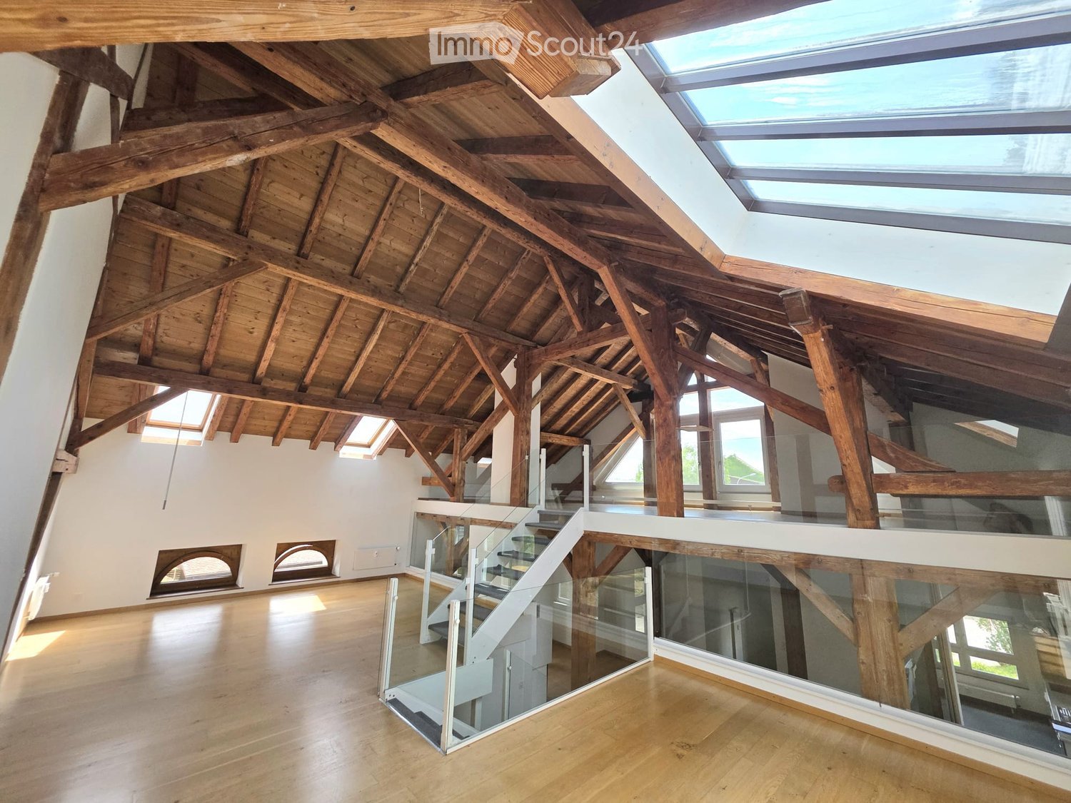 Open, airy space with exposed wooden beams and skylights, featuring a glass staircase leading to an upper level.
