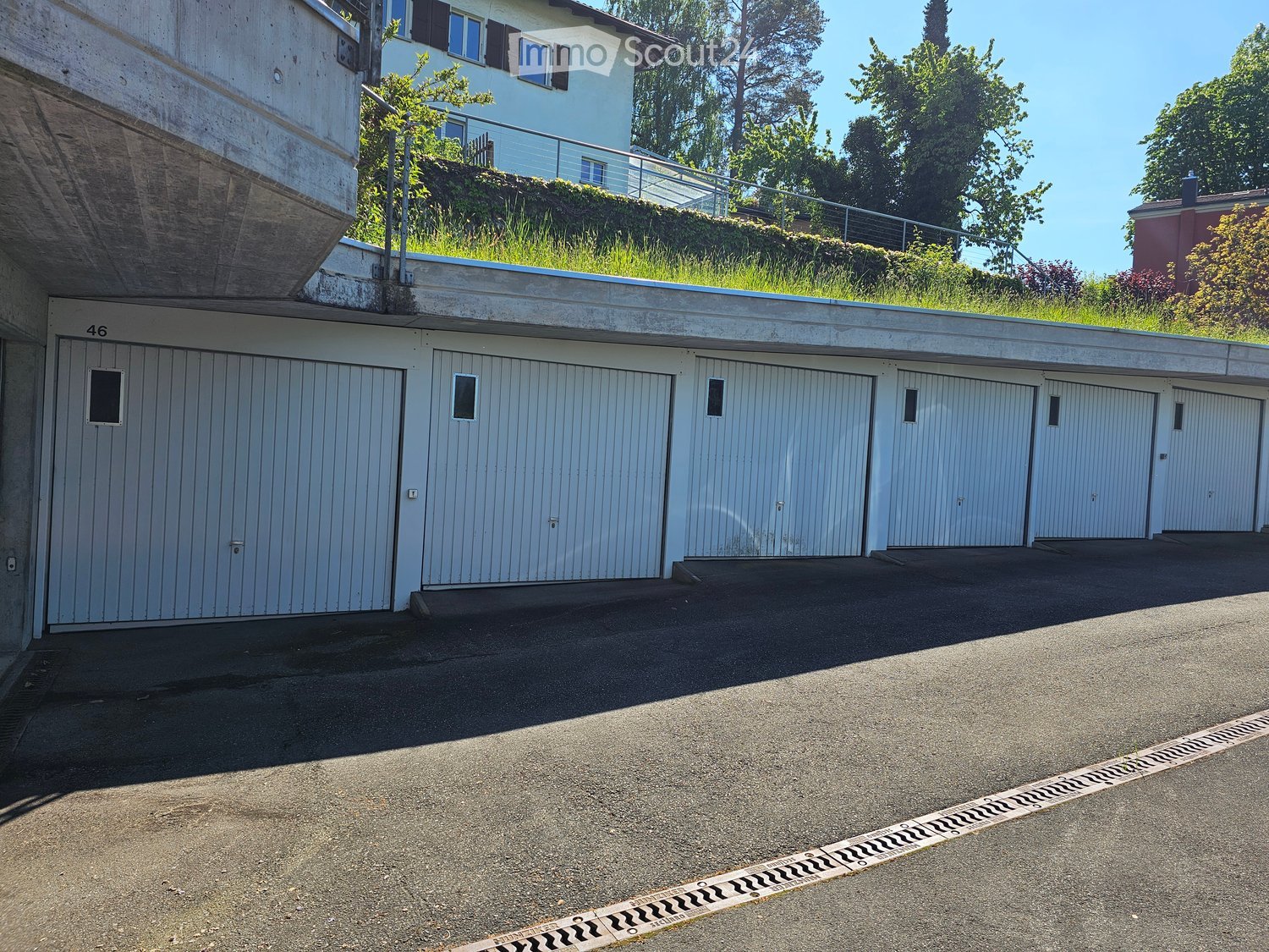 A multi-car garage with several closed garage doors, located under a raised ground floor with a grassy roof area and a staircase leading up to a house.