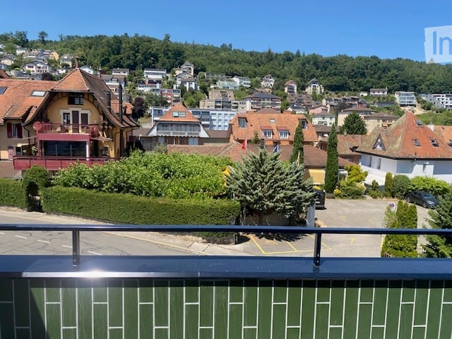Balcony overlooking a town with houses, trees, and a clear blue sky.