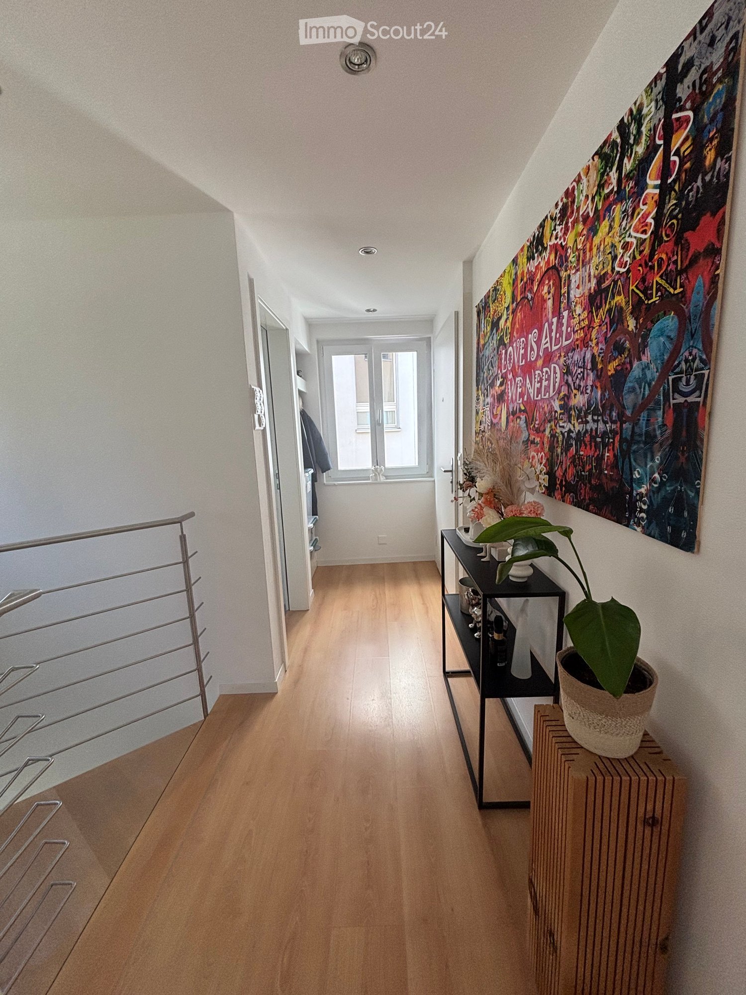 Hallway with wooden flooring, a black side table with a potted plant, and a colorful wall art piece.
