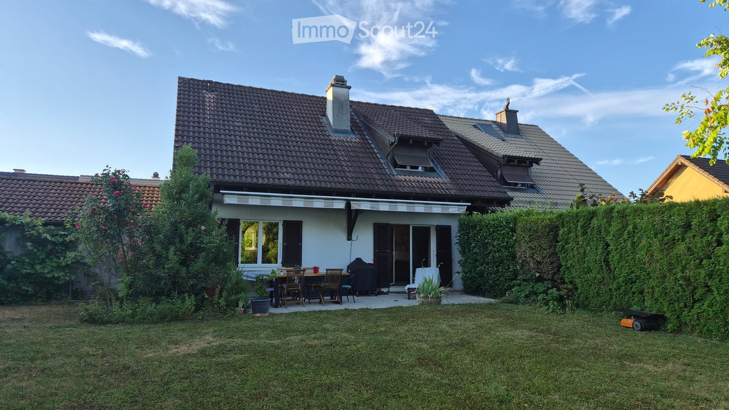 A well-maintained garden area in front of a house with a patio, outdoor furniture, and a lawn.