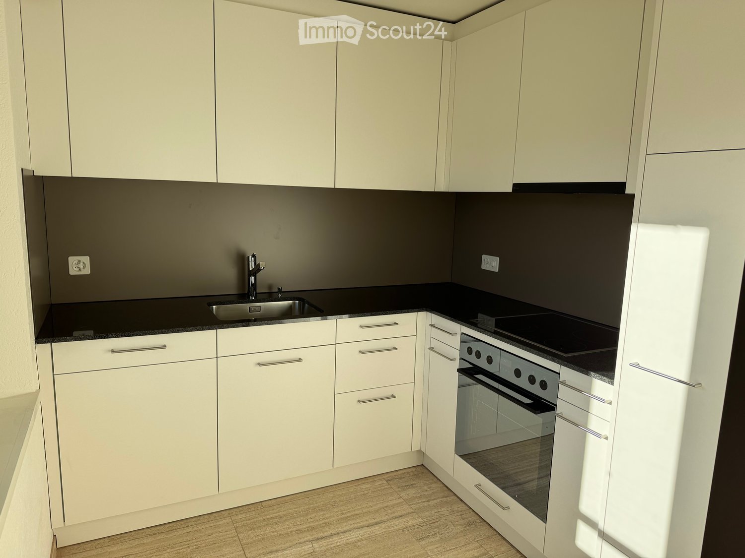 modern white kitchen with black countertops, silver sink, faucet, modern white cabinetry, oven, stove