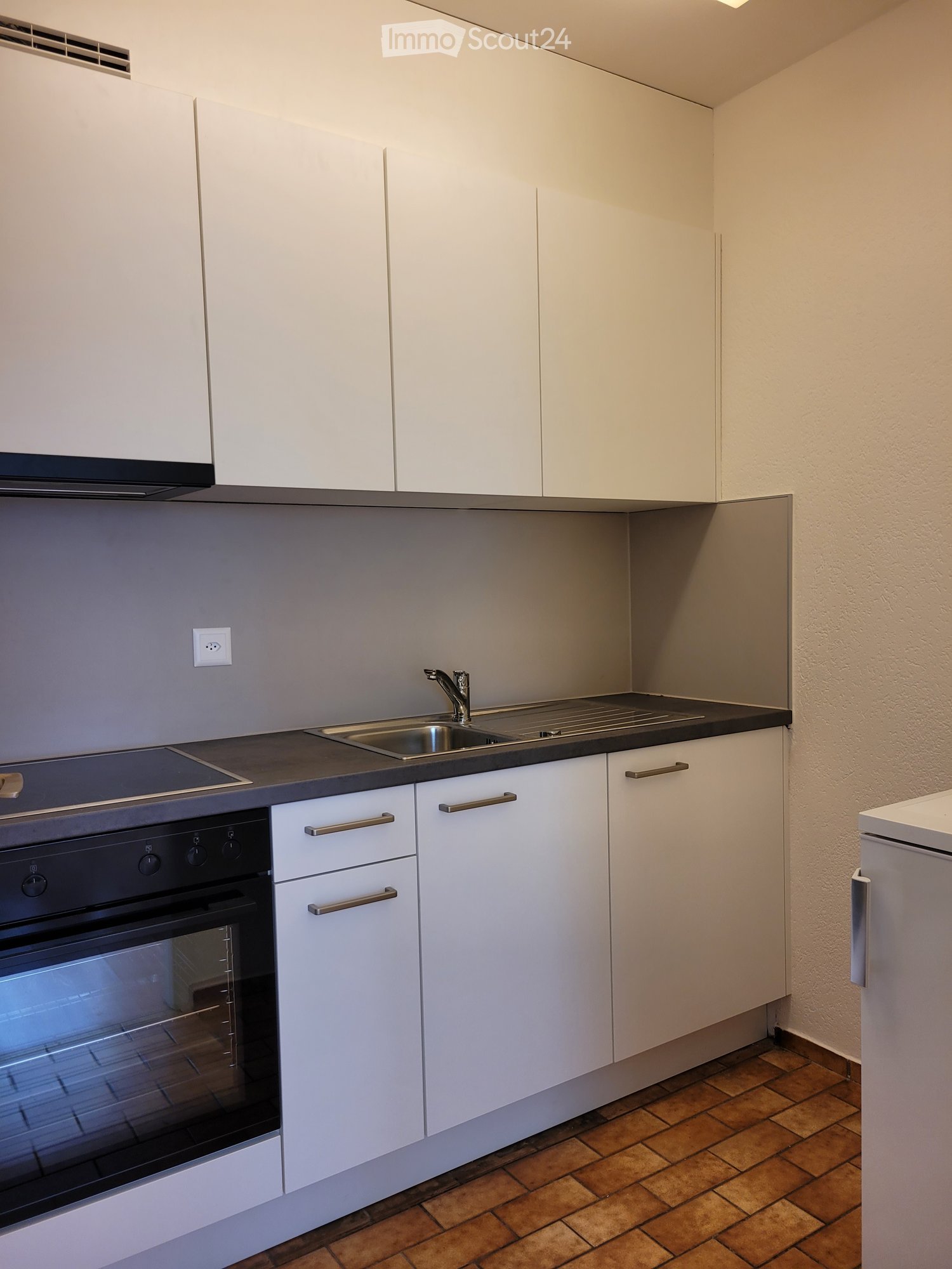 Modern kitchen with white cabinets, stainless steel sink, and built-in oven. Features a tiled floor and sleek design.