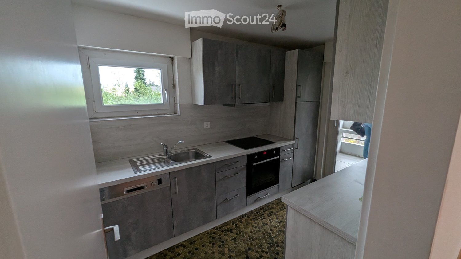 Modern kitchen with grey cabinets, stainless steel sink, oven, and dishwasher. Features a window with a view of greenery.