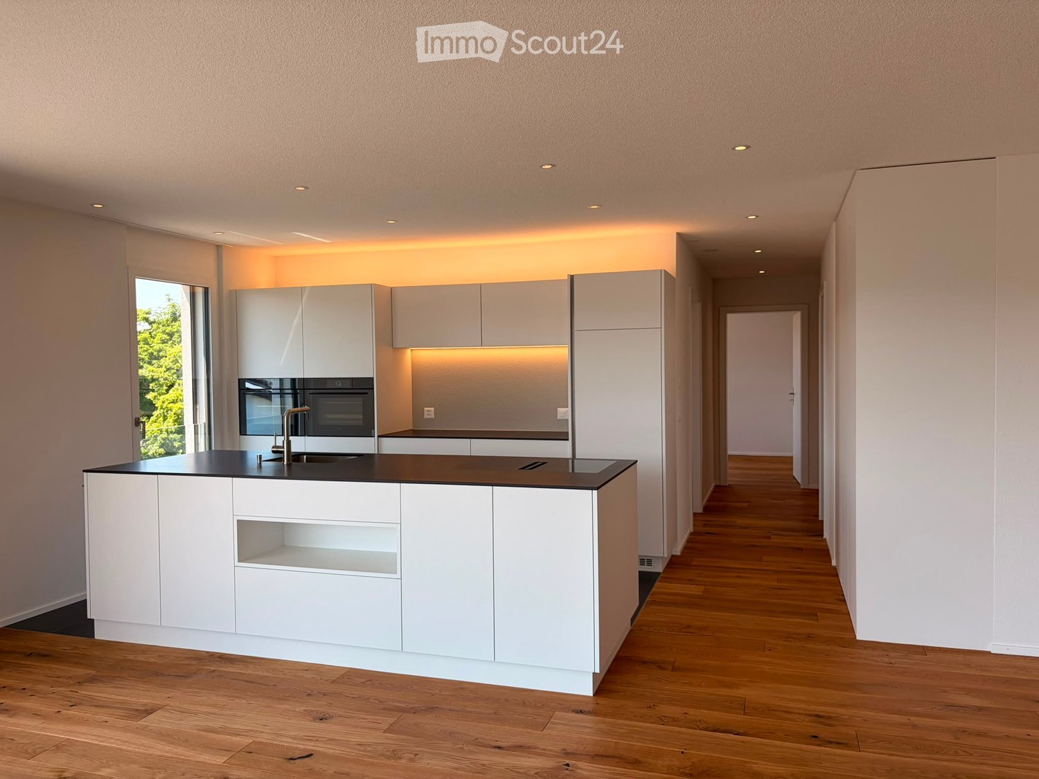 Modern kitchen with white cabinets, black countertop, and integrated appliances, featuring a sleek design and warm lighting.