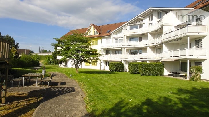 Apartment building with balconies, several floors, garden area, lawn, trees, pathway