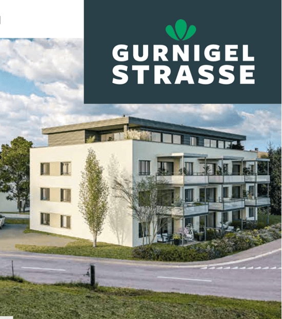 Modern multi-story residential building with balconies, large windows, and a contemporary design. The building features a clean, light-colored facade with a flat roof and is surrounded by greenery and a landscaped area.