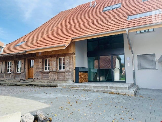 Two-story house with a red-tiled roof, stone and wooden facade, large glass entrance, and a paved driveway.