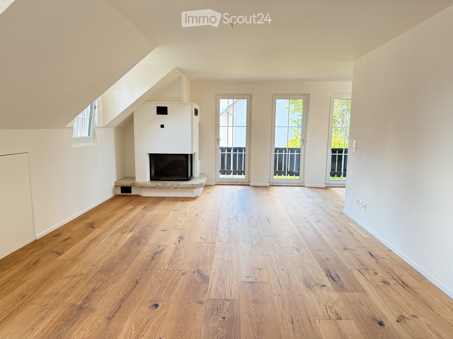 Empty room with wooden flooring, white walls, fireplace, and three large windows with glass doors leading outside.