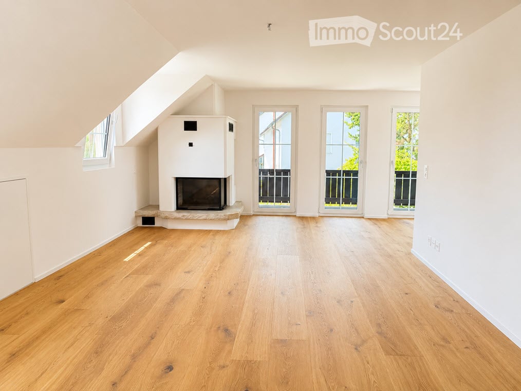 Bright, unfurnished room with wooden flooring, white walls, and a fireplace. Three large windows and doors lead to an outdoor area.