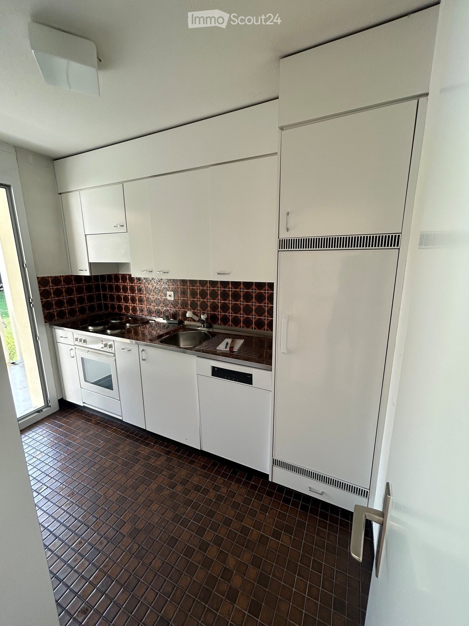 Modern kitchen with white cabinets, stainless steel appliances, and brown tiled flooring.