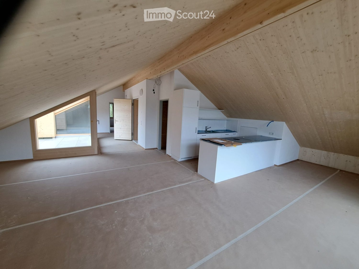 Empty attic space with wooden slanted ceilings, white walls, tiled floor, and a white kitchen island with cabinets and appliances.