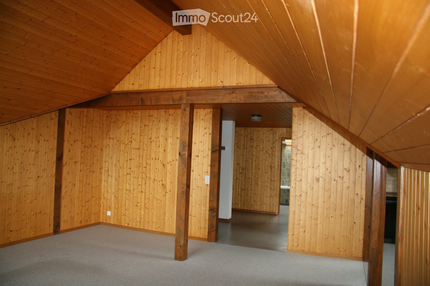 Empty attic space with wooden walls, exposed wooden beams, and a carpeted floor. No furniture or equipment is present.