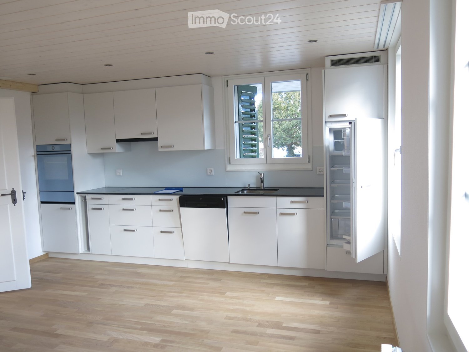 Modern kitchen with white cabinets, stainless steel appliances, and wooden flooring.