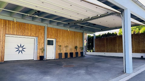 Modern garage with wooden paneling, white garage door, and small potted plants lining the entrance.